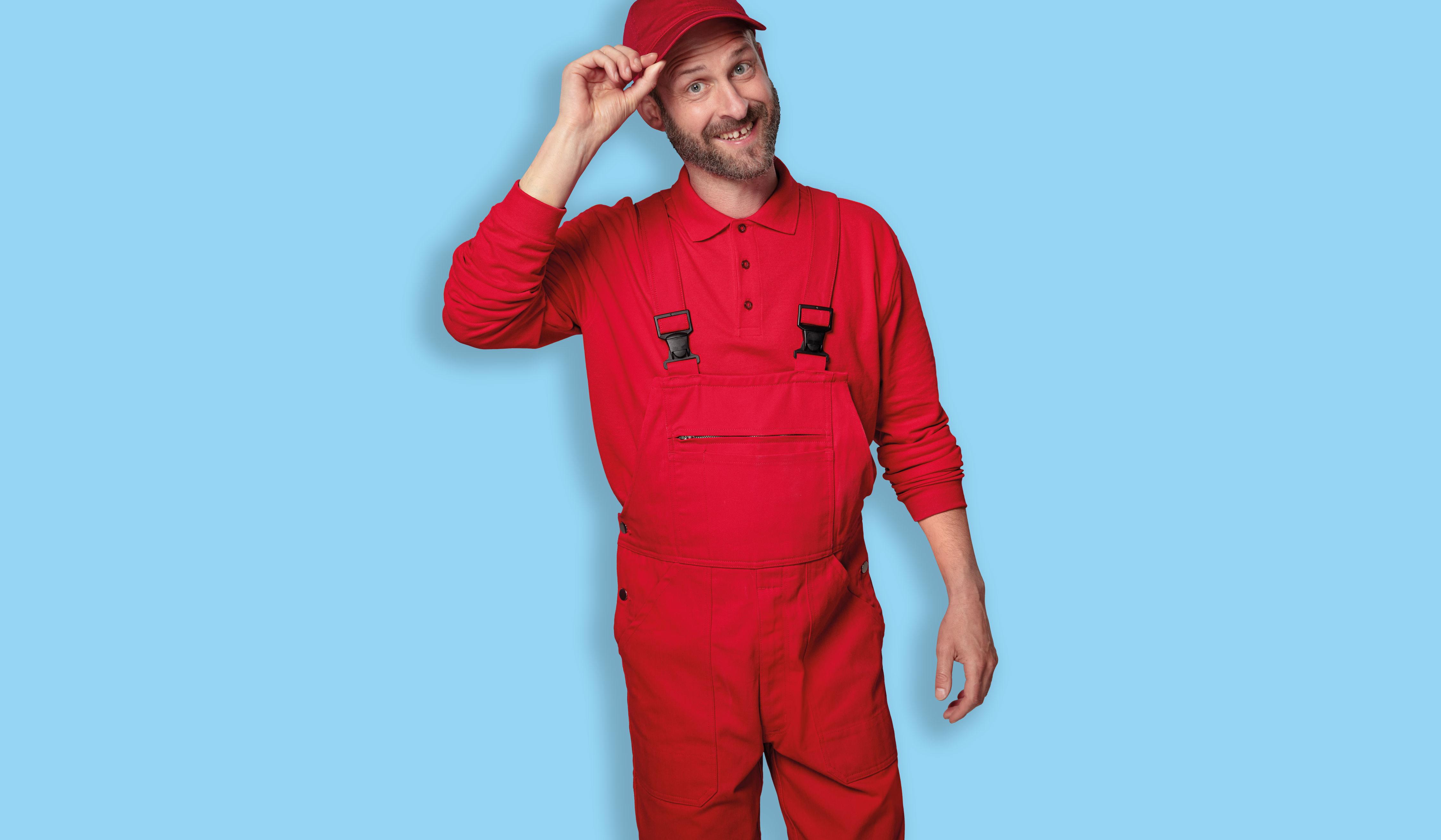 Mann in rotem Overall und roter Mütze lächelt vor hellblauem Hintergrund.