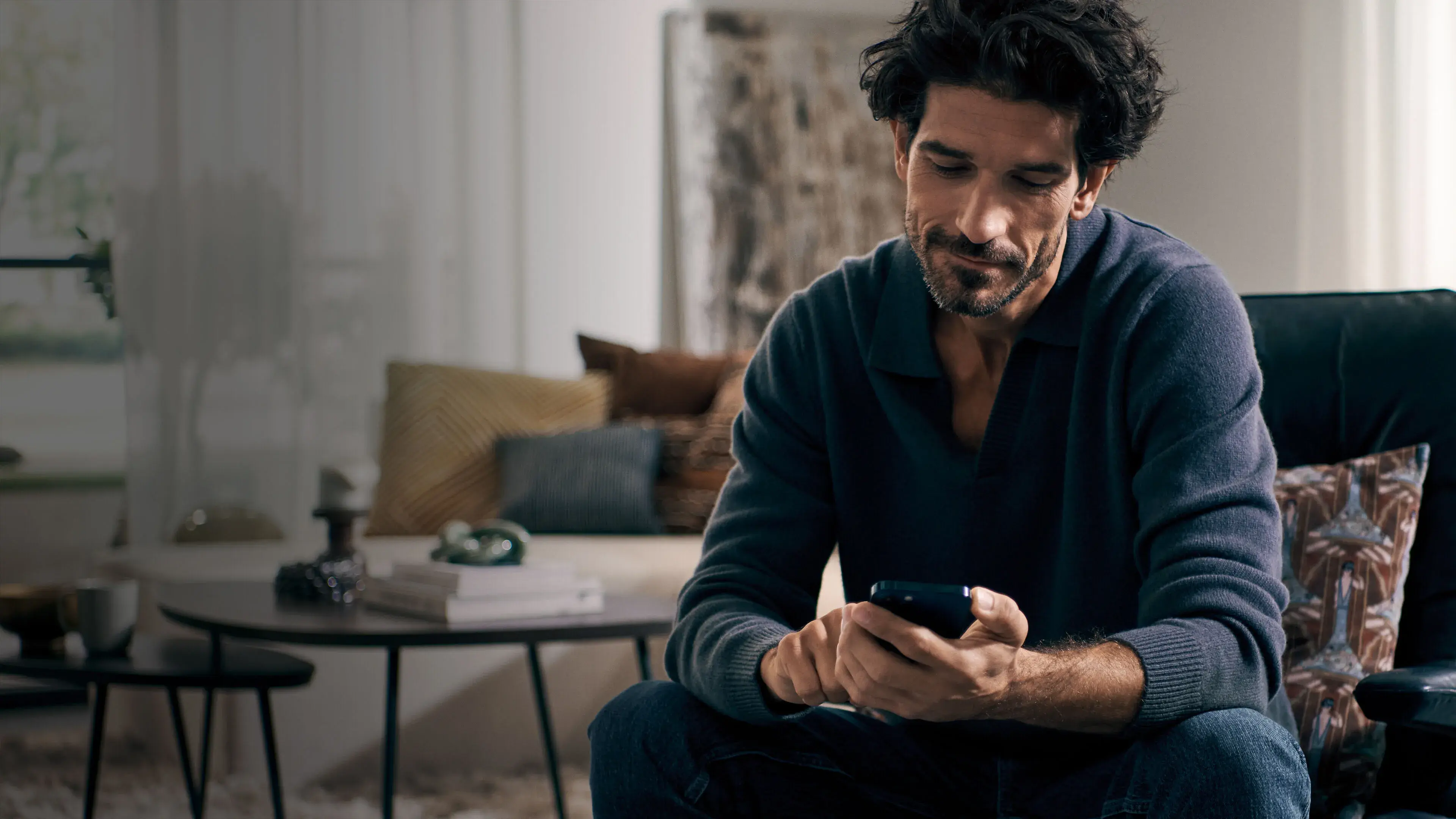 Siemens_Home_Appliances Mann sitzt auf Sofa und steuert via Smartphone seine Hausgeräte